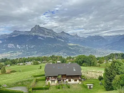 a house in a field with mountains in the background at Charmant duplex près du téléski du Bouchet, idéal pour famille - FR-1-560-11 in Combloux