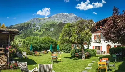 a garden with chairs and tables with a mountain in the background at Chalet-hôtel Gai Soleil in Les Contamines-Montjoie