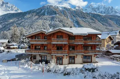 a log home in the snow with mountains in the background at Coin des Drus Apartment - Chamonix All Year in Chamonix-Mont-Blanc