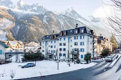 a large white building on a snowy street with mountains at Le Paradis 25 Apartment - Chamonix All Year in Chamonix-Mont-Blanc