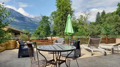 a patio with a table and chairs and a green umbrella at Petit chalet savoyard in Domancy