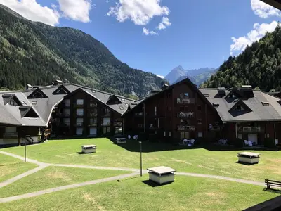a large building with benches in a field with mountains at Résidence L'enclave - Enclave I638 MAE-5354 in Les Contamines-Montjoie
