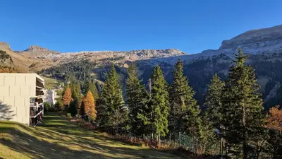 a building on a hill with trees and mountains at Résidence Les Pleiades - Appartement lumineux · Centre station · Balcon · Parking couvert MAE-7373 in Flaine