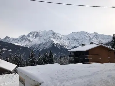 a house with snow on the roof with mountains in the background at Petite Marmotte in Saint-Gervais-les-Bains