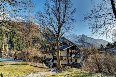 a building in the mountains with a tree in the foreground at MGM Parc Couttet in Chamonix-Mont-Blanc