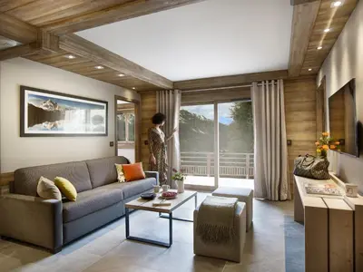 a living room with a couch and a person looking out the window at MGM Hôtels & Résidences - Résidence Chalets Laska in Les Contamines-Montjoie