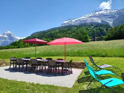 a group of tables and chairs with red umbrellas and mountains at Le clair logis in Sixt