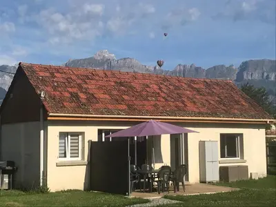 a house with an umbrella and a table and chairs at maisonnette entre lac de Passy et montagnes in Domancy