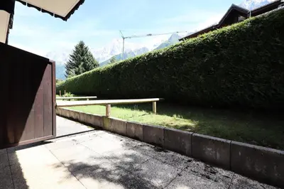 a bench in front of a hedge with mountains in the background at Résidence Les Eaux Rousses - Les Eaux Rousses MAE-9964 in Les Houches