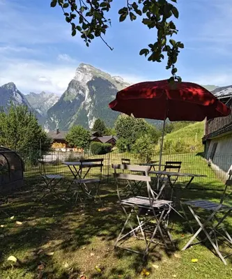 a table and chairs with a red umbrella and mountains at Le Battieu in Samoëns