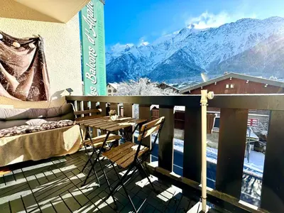 a balcony with a table and a couch and mountains at Appartement vue Montblanc 5mn piste1 in Les Houches