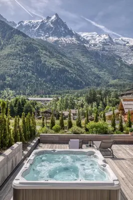a hot tub on a deck with mountains in the background at Chalet Rytola, modern & central chalet in Chamonix in Chamonix-Mont-Blanc