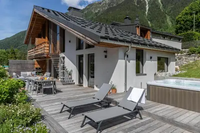 a house with a deck with chairs and a hot tub at Chalet Rytola, modern & central chalet in Chamonix in Chamonix-Mont-Blanc