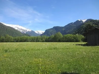 an open field with a barn and mountains in the background at Appartement de 6 personnes avec terrasse, parking et Wi-Fi - FR-1-629-25 in Samoëns