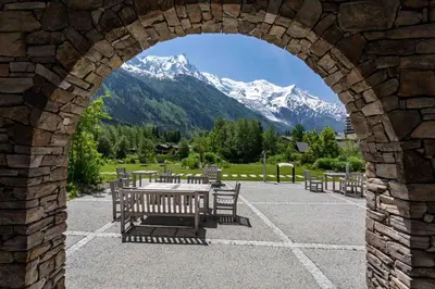 an archway with a table and benches with mountains in the background at La Cordee 703 Apartment - Chamonix All Year in Chamonix-Mont-Blanc