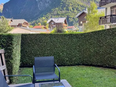 a chair sitting in the grass next to a hedge at Studio lumineux au centre, jardin, parking, casier à skis - FR-1-624-56 in Samoëns