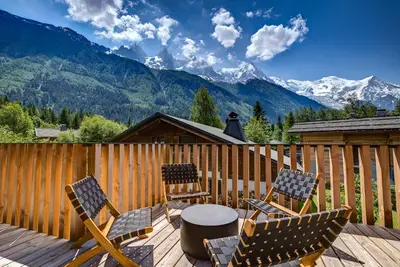 two chairs and a table on a deck with mountains at Chalet Breitalps in Chamonix-Mont-Blanc