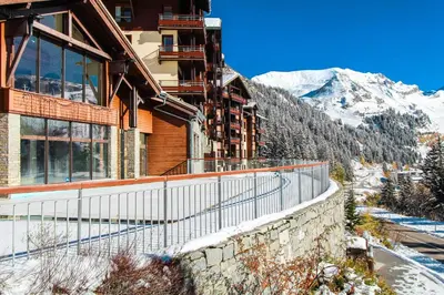 a building with a fence next to a mountain at Cosy, modern 2-bed with fireplace & beautiful views in Flaine