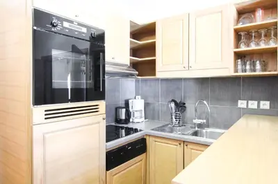 a kitchen with wooden cabinets and a black appliance at Two internally connecting 2-bed apartments with shared private entrance in Flaine