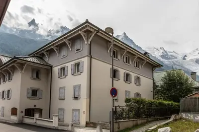 a large white building with mountains in the background at Villa Vallet- Newly renovated 2 bedroom nestled just off the main street in Chamonix-Mont-Blanc