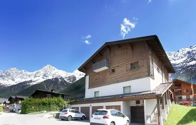 two cars parked in front of a building with snow covered mountains at Les Alpages - Newly Renovated - 2bed - Equipment Storage - Mont-Blanc Views in Les Houches