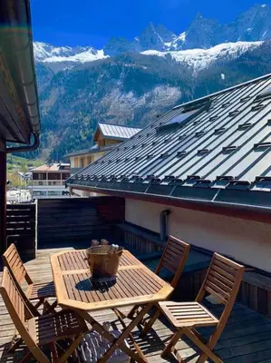 a wooden table and chairs on a balcony with mountains at 90m2 hypercentre, terrace, next to ski lift in Chamonix-Mont-Blanc