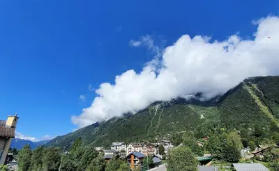 a town in front of a mountain with clouds at La Rivière - Aiguille du Midi in Chamonix-Mont-Blanc