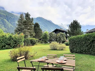 a wooden picnic table with chairs and mountains in the background at Chamonix Appartement Vue Mont Blanc avec jardin in Chamonix-Mont-Blanc