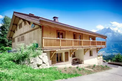 a large wooden house with a balcony and mountains at La Ferme des Fingères in Cordon