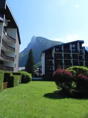 a building with a green yard with a mountain in the background at Samoëns - Studio Les Espaces in Samoëns