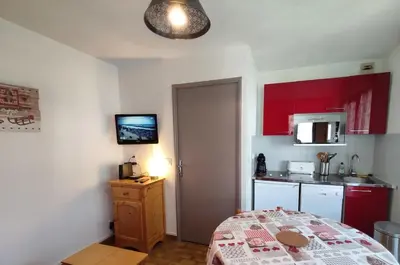 a small kitchen with red cabinets and a bed in a room at Samoëns - Studio Les Espaces in Samoëns