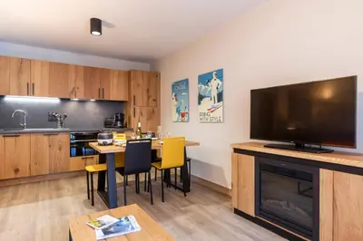 a living room with a kitchen with a table and a television at Résidence Club MMV Samoens Village in Samoëns