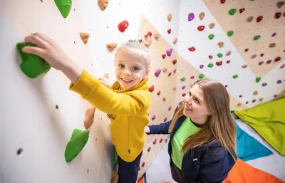 a young girl helping a child on a climbing wall at Résidence Club MMV Samoens Village in Samoëns