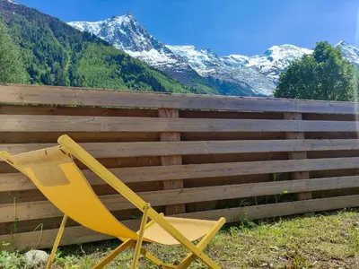 a yellow chair sitting next to a fence with snow covered mountains at Les Cîmes du Mont-Blanc in Chamonix-Mont-Blanc