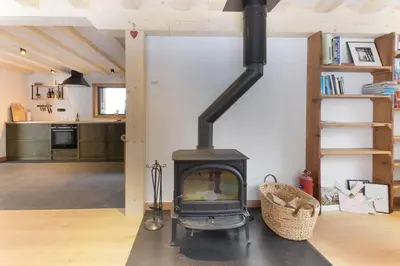 a wood stove in a living room with a kitchen at Chalet L'Oratoire & Mazot - Renovated Historic Chalet - Huge Garden & Separate Cabin for 2 in Les Houches
