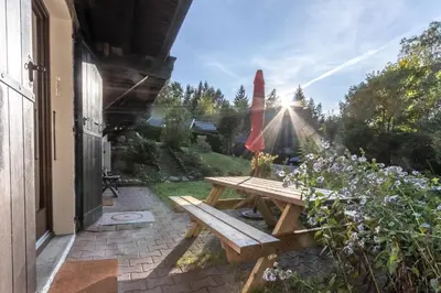 a wooden picnic table on a patio with the sun shining at Clos de l'Ours - 2 chambres - Jardin privé in Chamonix-Mont-Blanc