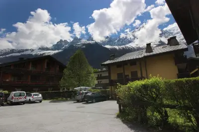 a building with cars parked in a parking lot with mountains at Les Gaillands in Chamonix-Mont-Blanc
