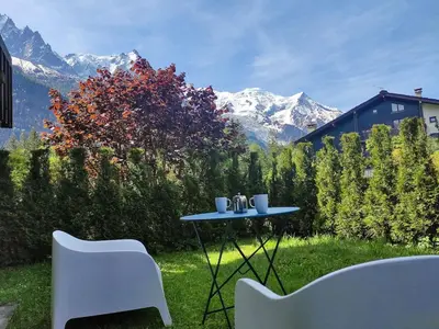 a table and chairs on a lawn with mountains in the background at Le Jardin de Champraz in Chamonix-Mont-Blanc