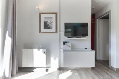 a white living room with a tv on a wall at Le Jardin de Champraz in Chamonix-Mont-Blanc