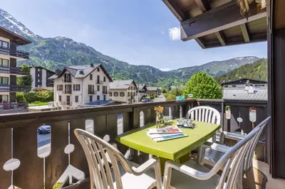 a green table and chairs on a balcony with mountains at Appartement Central Des Houches - 15 - Happy Rentals in Les Houches