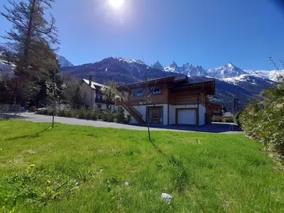 a house in the mountains with a green field at Chalet Lily by Brennus Chamonix in Chamonix-Mont-Blanc
