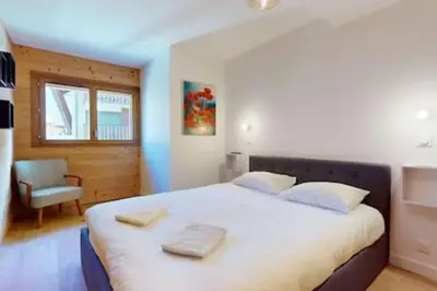 a bedroom with a large white bed with a chair at Les Carlines 09 in Samoëns