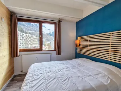 a bedroom with a bed with a blue wall and a window at Appartement Confortable, Proche Pistes & Commerces, Balcon - FR-1-425-144 in Flaine