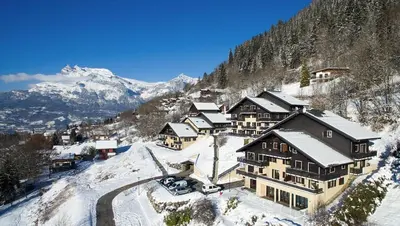 a building on a snowy hill with snow covered mountains at Appartement dans châlet avec piscine couverte in Saint-Gervais-les-Bains