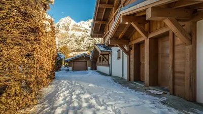 a snow covered alley with buildings and mountains in the background at Chalet du Bois in Chamonix-Mont-Blanc