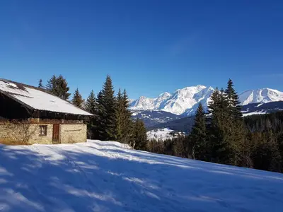 a snow covered house with mountains in the background at Appartement - Combloux in Combloux