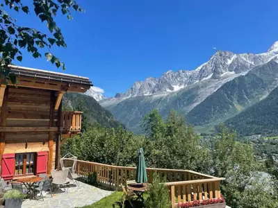a log cabin with a deck and mountains in the background at Chalet 3 étoiles pour 4 pers avec vue imprenable sur la vallée de Chamonix in Les Houches