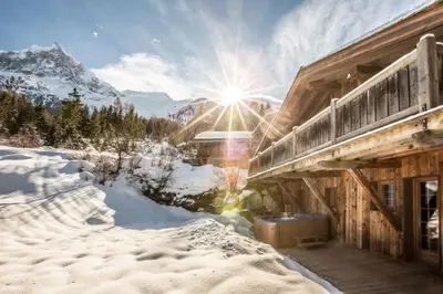 a snow covered building with the sun in the background at Chalet l'Ourson, avec jacuzzi, sauna, services hôteliers in Chamonix-Mont-Blanc