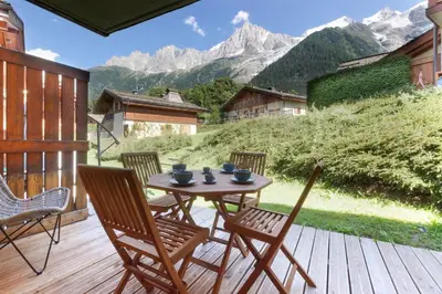 a table and chairs on a wooden deck with mountains at Les Granges des Bossons in Chamonix-Mont-Blanc