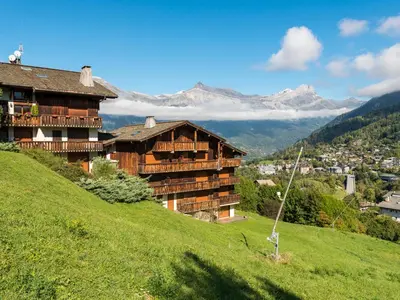 a building on a hill with mountains in the background at Ski-in/ski-out & pool: great for summer and winter in Saint-Gervais-les-Bains